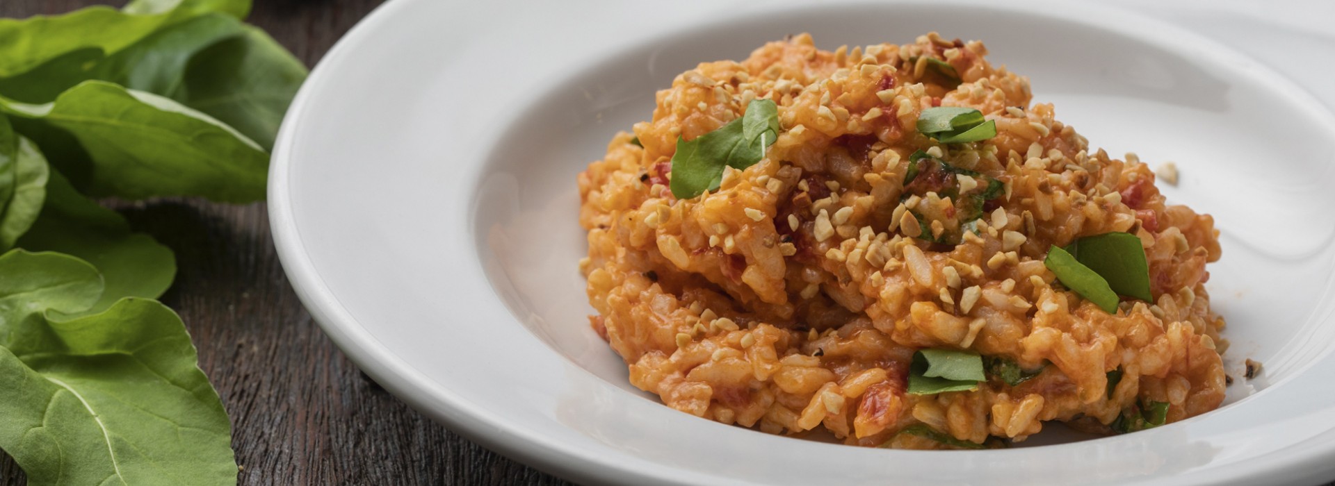 Risoto cremoso com tomate, castanhas e folhas frescas servido em prato branco