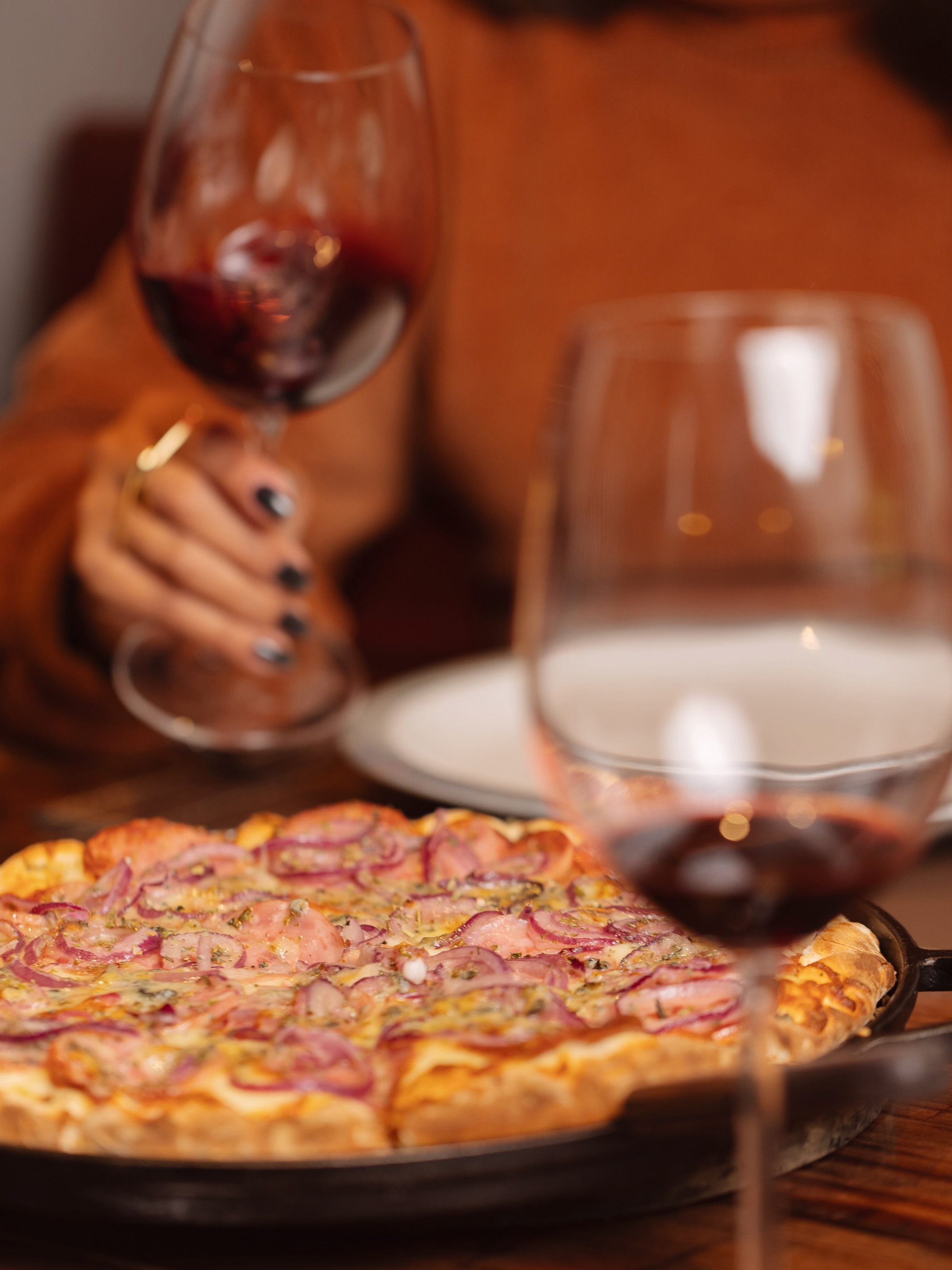 Pizza servida na mesa da Pizza Entre Vinhos ao lado de duas taças de vinho tinto