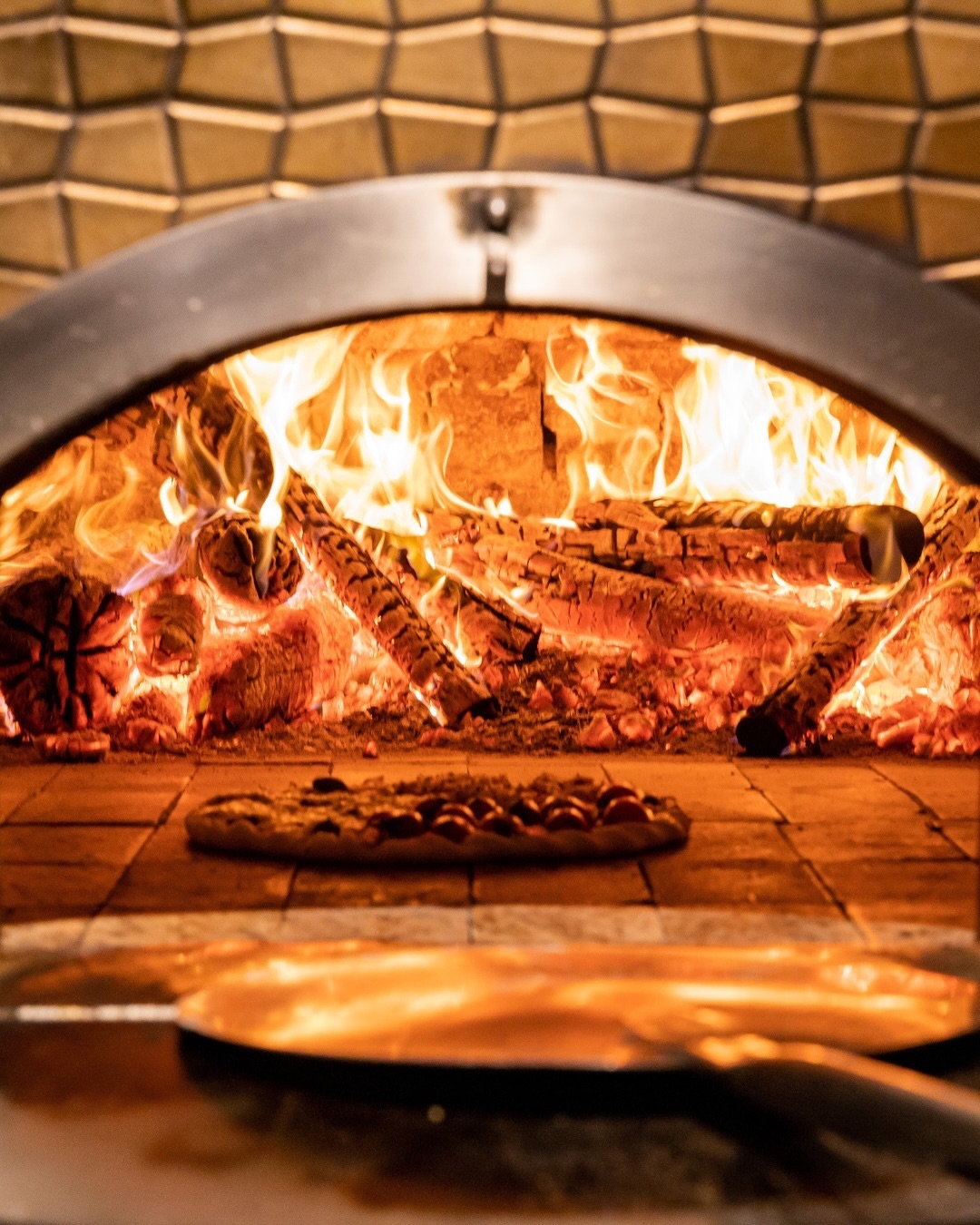 Forno a lenha aceso da Pizza Entre Vinhos com uma pizza assando sobre o piso de pedra